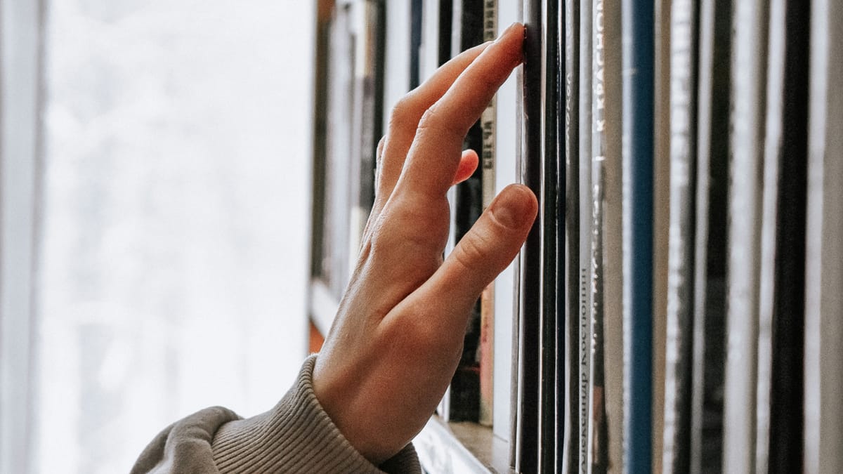 Woman's hand touching lightly the cover of a book on a book shelf.